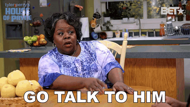 a woman sits at a table with the words go talk to him written on the bottom