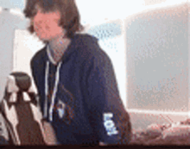 a man in a blue hoodie is standing next to a dog in a room .