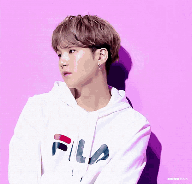 a man wearing a white fila hoodie stands in front of a purple wall