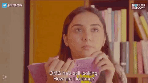 a girl is holding a book in front of her face and talking to a man .