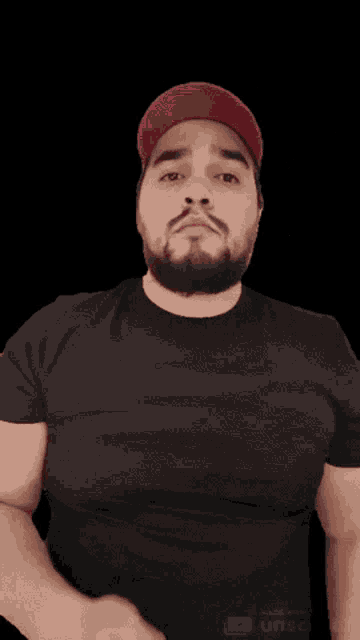 a man with a beard wearing a black shirt and a red hat giving a thumbs up