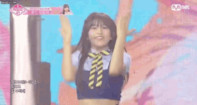 a girl in a crop top and tie is dancing on a stage with her arms in the air .