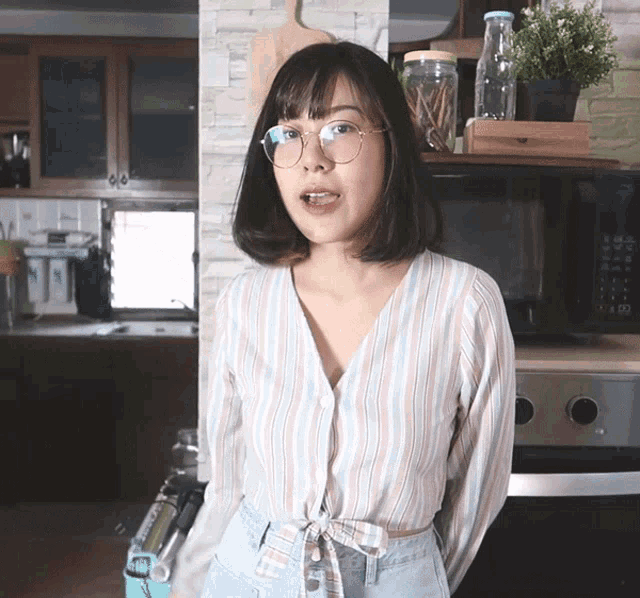 a woman wearing glasses and a striped shirt stands in front of a microwave oven