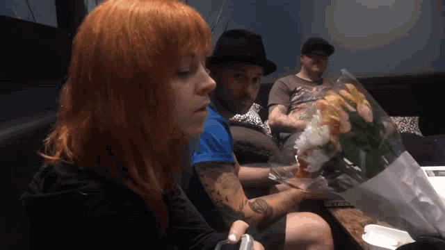 a woman with red hair holds a bouquet of flowers in front of two men