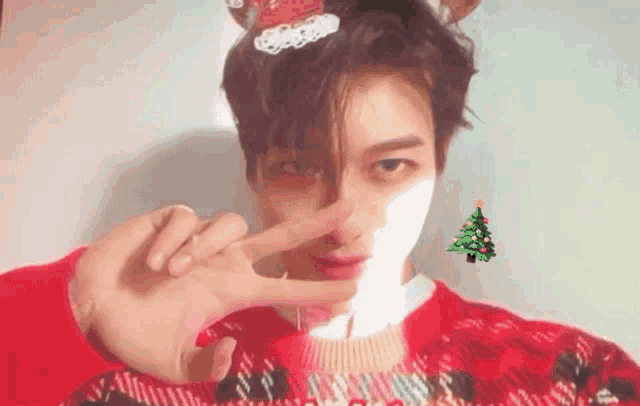 a man wearing a red sweater with a christmas tree on it makes a peace sign