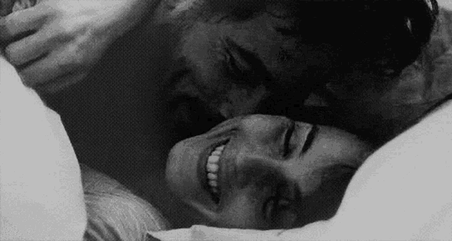 a black and white photo of a man kissing a woman on the forehead in bed .