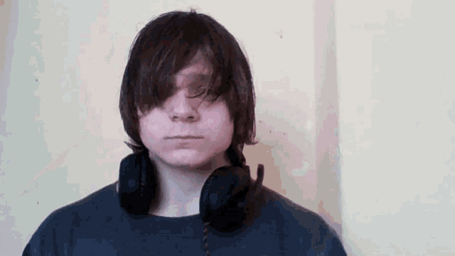a young man with headphones around his neck looks at the camera with his eyes closed