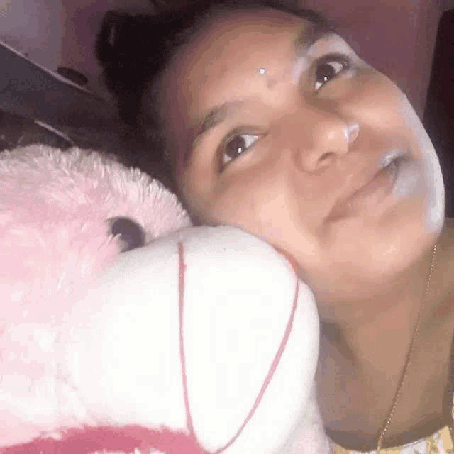 a woman is laying down with a pink teddy bear on her chest .