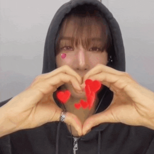 a man in a black hoodie is making a heart shape with his hands .