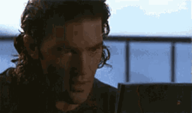 a man with long hair is looking at a laptop screen .