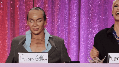 two drag queens sitting at a table with a sign that says gilbert + gottfried