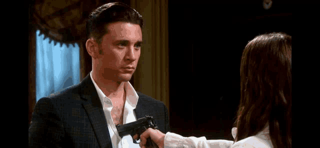 a man in a suit is holding a gun in front of a woman .
