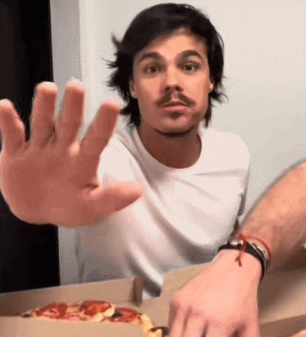 a man in a white shirt is reaching out his hand towards a box of pizza