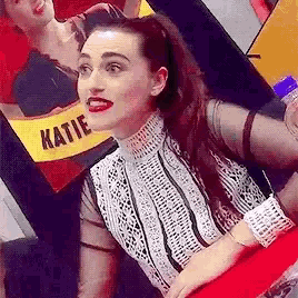 a woman in a red dress is sitting in front of a sign that says katie .