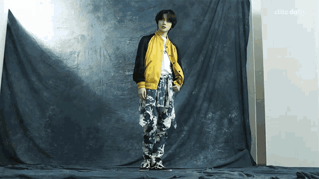 a man in a yellow jacket stands in front of a blue cloth that says elite daily on it