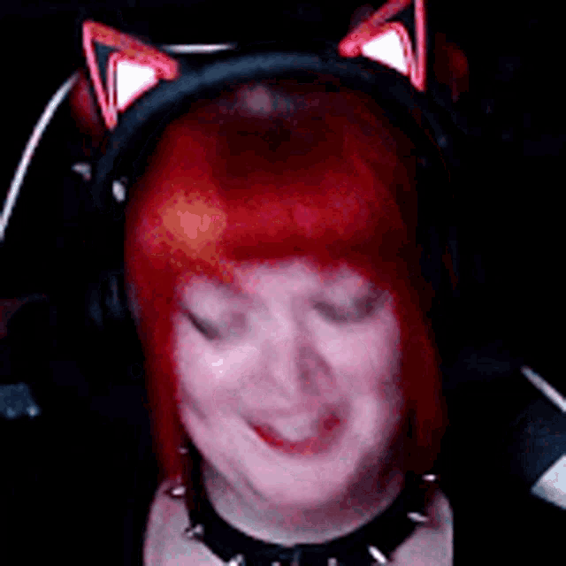 a woman with red hair is wearing headphones and a choker and smiling .