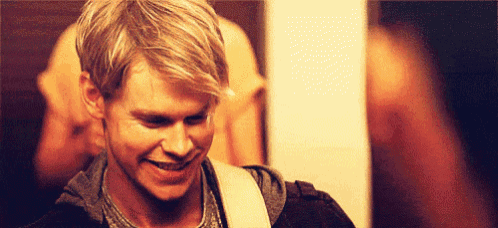 a man with blonde hair is smiling while playing a guitar .