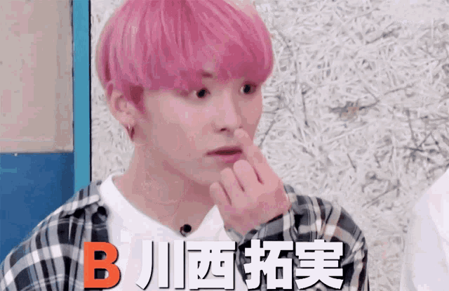 a young man with pink hair holds his nose in front of a sign that says b.