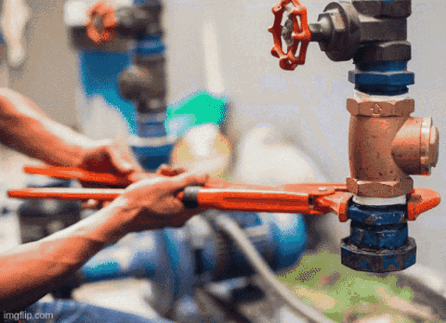 a man is fixing a pipe with a wrench and a red handle