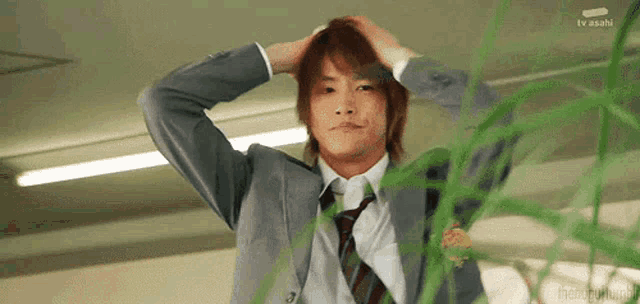a man in a suit and tie holds his hand to his head in front of a tv screen that says tv asahi