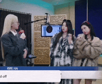 a woman in a fur coat talks into a microphone in a room