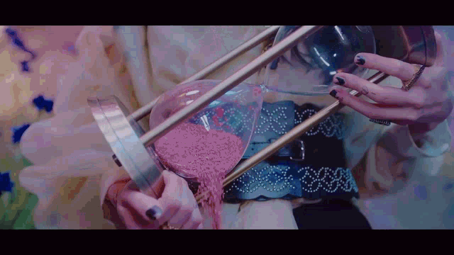 a woman holds a hourglass with pink sand pouring out of it