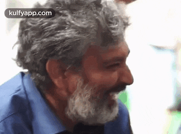 a man with a beard and a blue shirt is smiling and laughing .