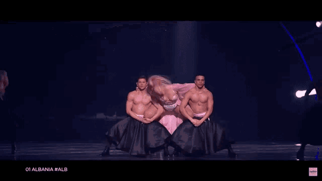 a woman in a pink dress is surrounded by two shirtless men and the caption 01 albania # alb