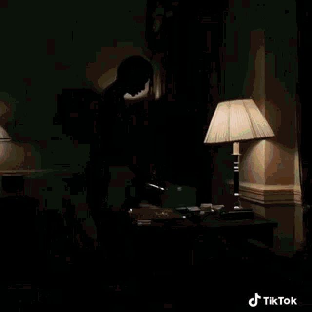 a man standing in front of a desk with a lamp and a box that says tiktok on the bottom