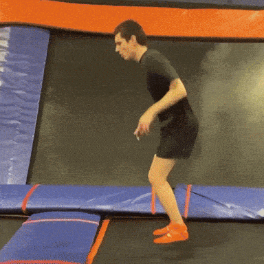 a man is jumping on a trampoline wearing shorts and a black shirt