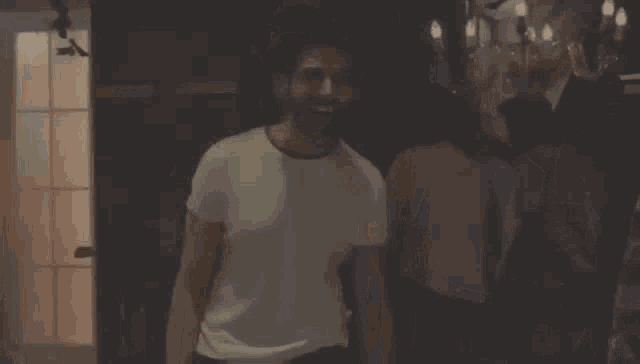 a man in a white t-shirt is dancing in a room in front of a mirror .
