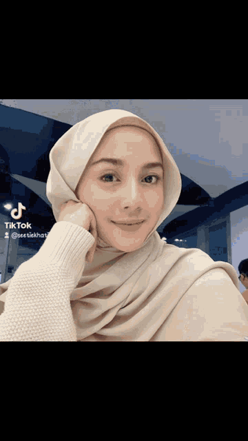 a woman wearing a hijab and a white sweater has tiktok written on the bottom right corner
