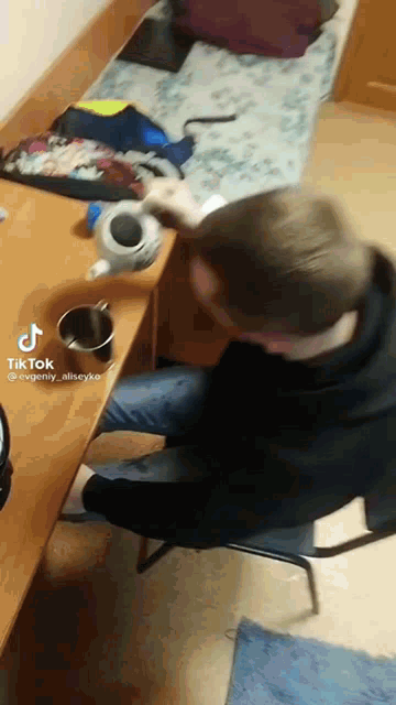 a man is sitting at a desk with a cup of coffee and a tik tok sticker on the bottom right