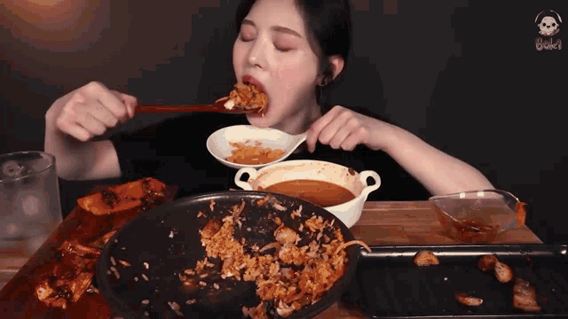 a woman is eating a spoonful of food from a bowl on a table