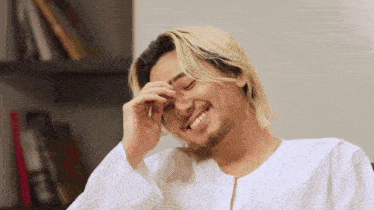 a man with long blonde hair and a beard is smiling and rubbing his forehead .