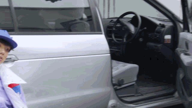 a boy in a blue hat is standing in front of a silver car