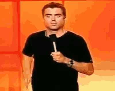 a man in a black shirt is holding a microphone in front of an orange background .