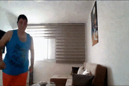 a man in a blue tank top is standing in front of a couch