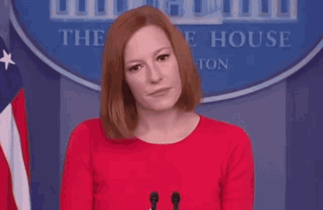a woman in a red dress is standing in front of a microphone in front of a white house sign .