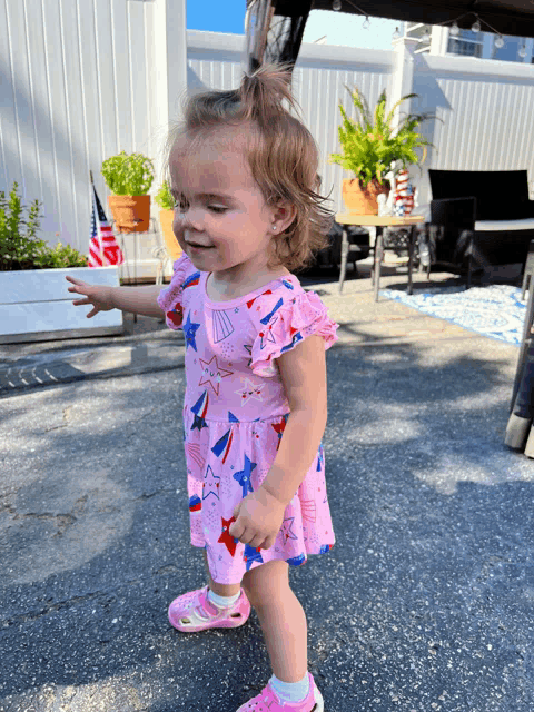 a little girl wearing a pink dress with red white and blue stars on it