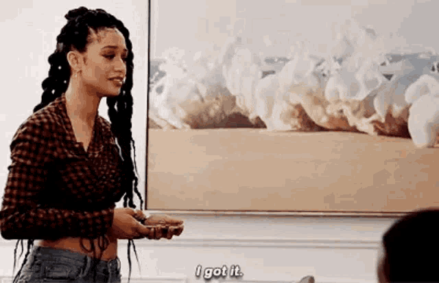 a woman in a plaid shirt is standing in front of a painting and holding a cell phone .