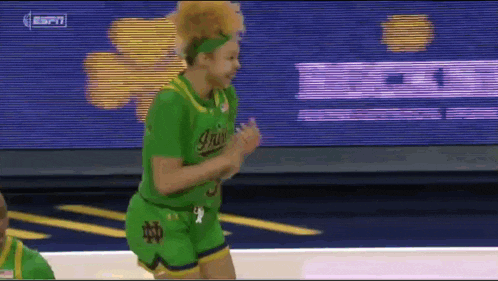 a female basketball player wearing a green jersey and shorts is dancing on the court .