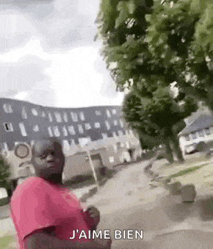 a man in a pink shirt is standing in front of a building and trees .