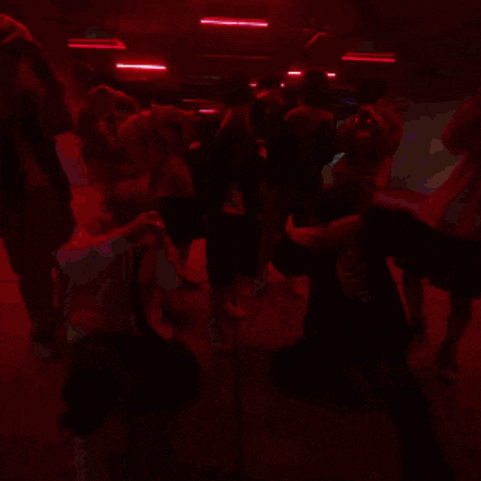 a group of people are dancing in a dark room and one of them is wearing a skeleton jacket