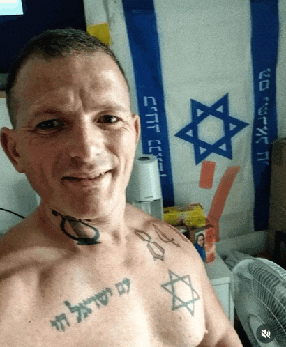 a shirtless man with a tattoo on his chest stands in front of a flag