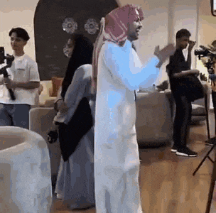 a man in a white robe is standing in a living room with a woman in a hijab .