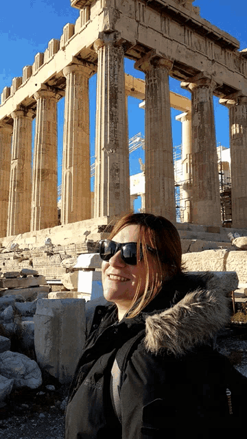 a woman wearing sunglasses is smiling in front of a very old building
