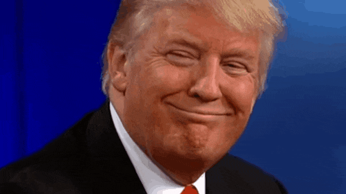 donald trump is smiling and making a funny face in front of a blue background .