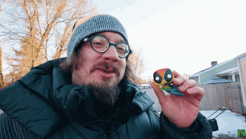 a man wearing glasses and a beanie holds a deadpool funko pop