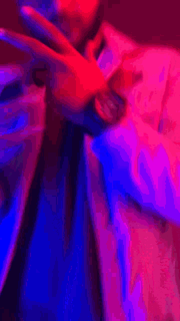 a man is making a peace sign with his hand in a pink and blue light